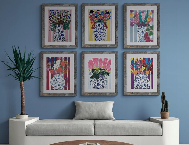 Living room with a gray sofa, wooden coffee table, and six framed coordinated paintings of floral bouquets in blue and white ginger jars on a striped background by Pink Sapphire Designs.