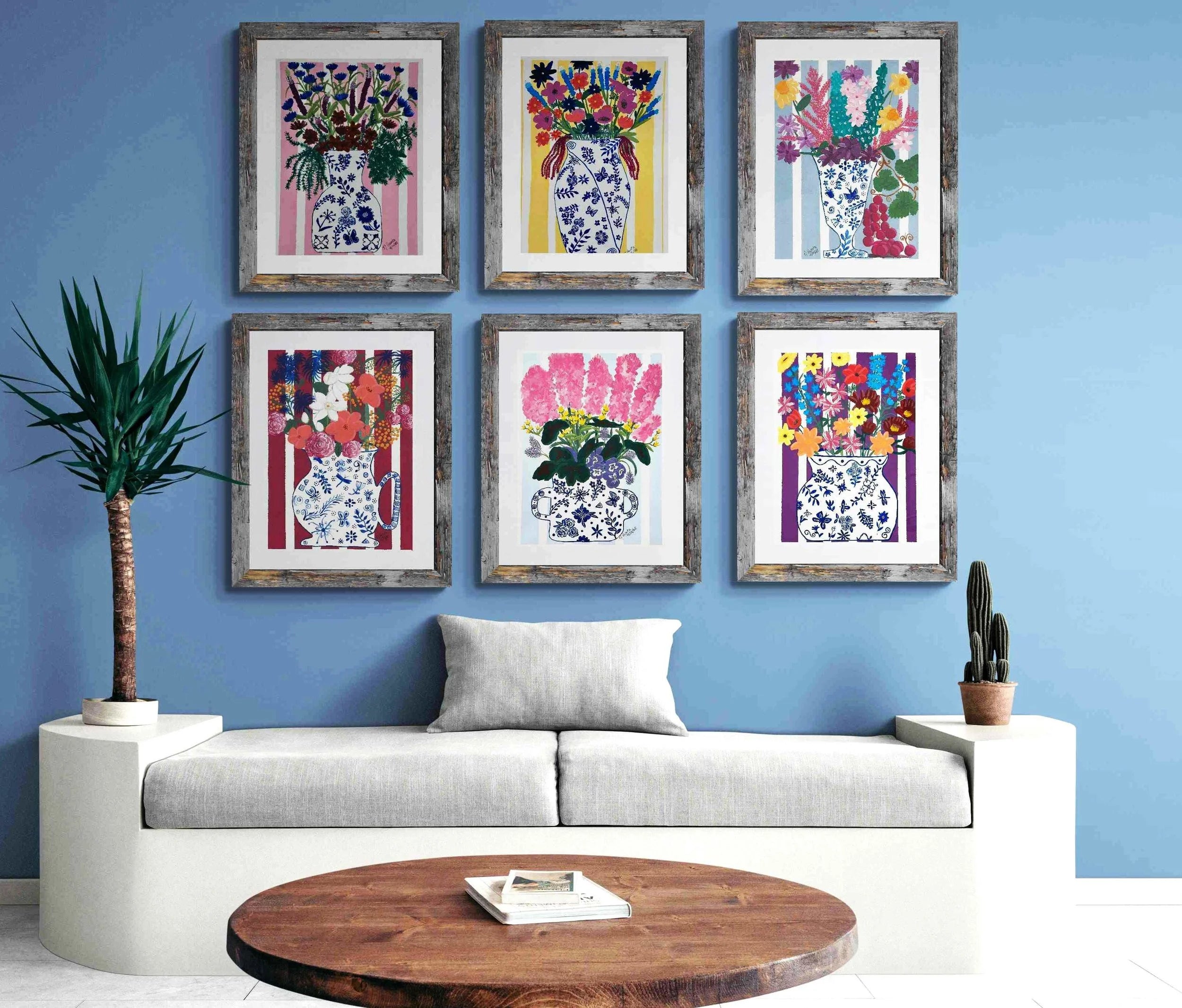 Living room with a blue wall, gray sofa, wooden coffee table, and 6 framed artworks of floral boquets in blue and white chinoiserie style vases.