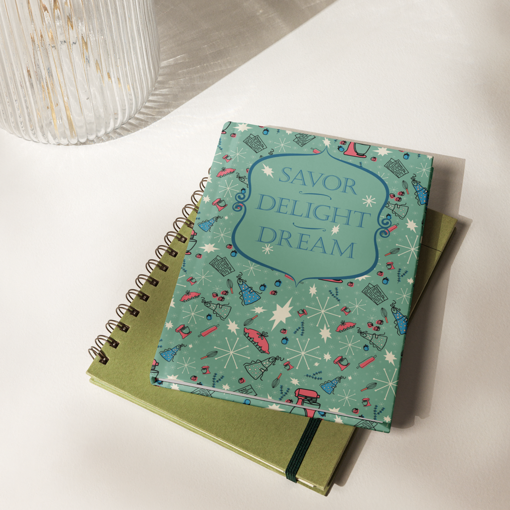 Closed Savor, Delight, Dream hardcover journal stacked on top of a green spiral notebook