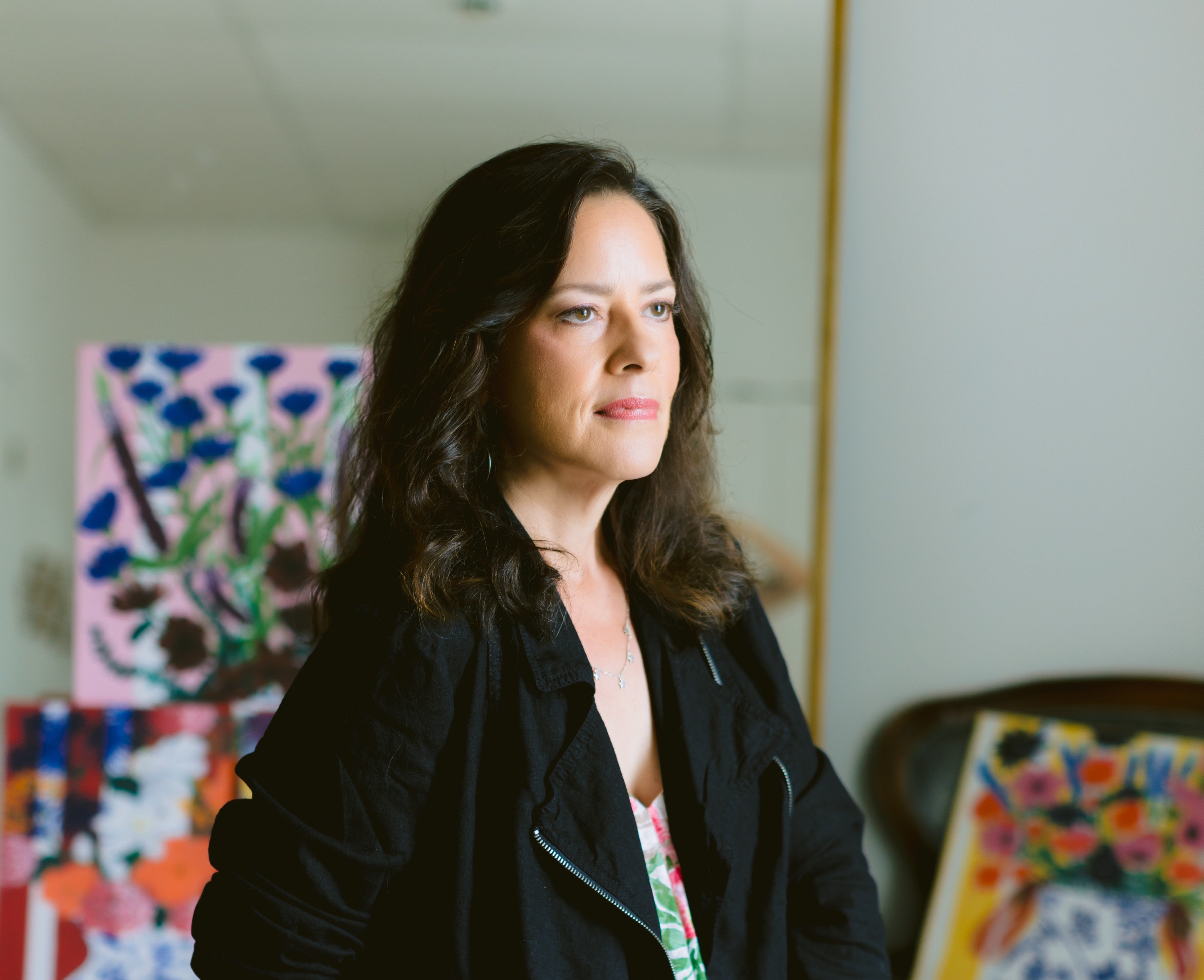 Female artist standing in a room with colorful abstract paintings on the wall.
