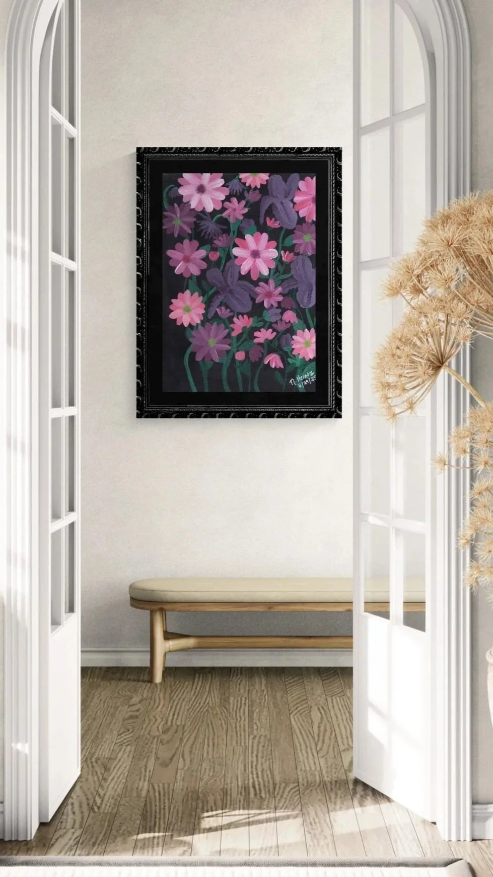 Floral painting with purple bearded irises and pink blossoms on a black background with a black frame, hung on a white wall in a room with wooden flooring and a bench.